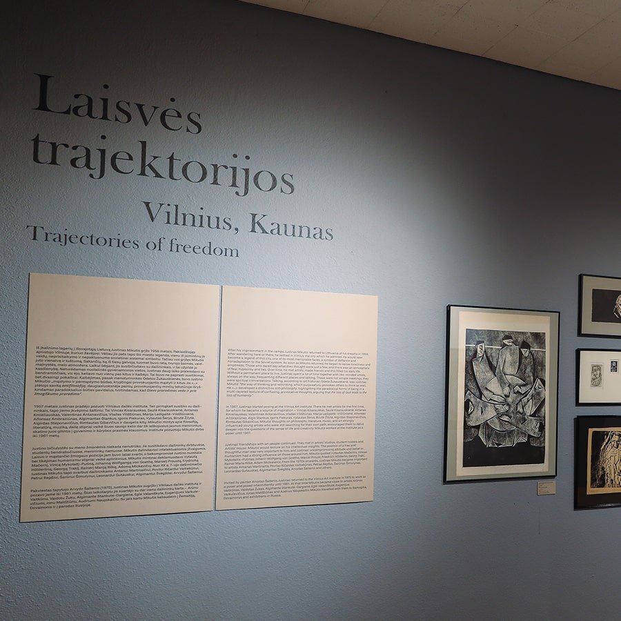 Exhibition wall with the title “Laisvės trajektorijos: Vilnius, Kaunas / Trajectories of Freedom” alongside framed monochrome artworks and curatorial text panels.