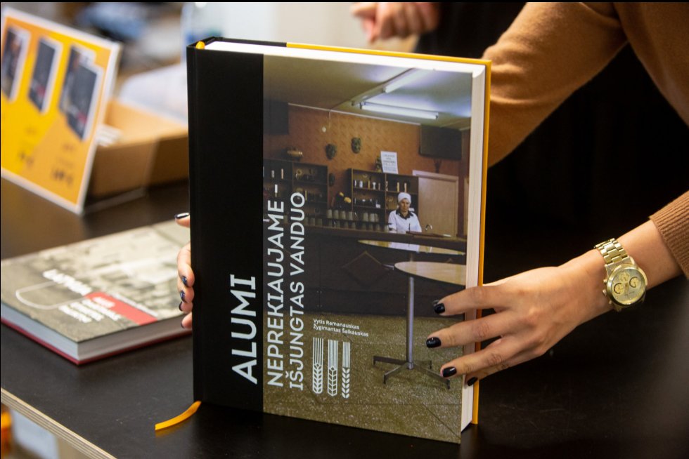 A person holds a large book titled “No Beer for Sale — The Water’s Been Cut Off,” featuring a photograph of a historic bar interior on the cover.