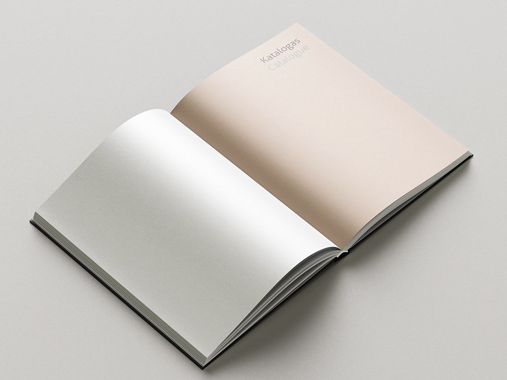 Open catalogue at a section divider. The right-hand page has a pale beige background and the heading “Katalogas / Catalogue,” while the facing page is blank.