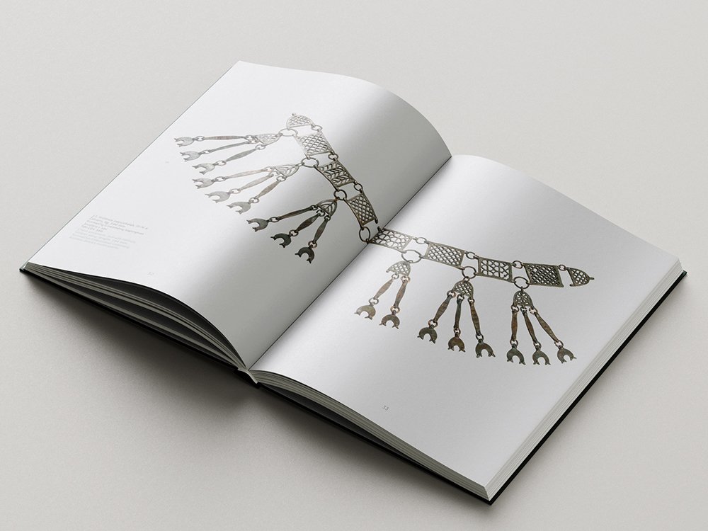Open catalogue spread presenting an ornate archaeological metal object composed of linked decorative plates, rings and multiple hanging elements, photographed across both white pages.