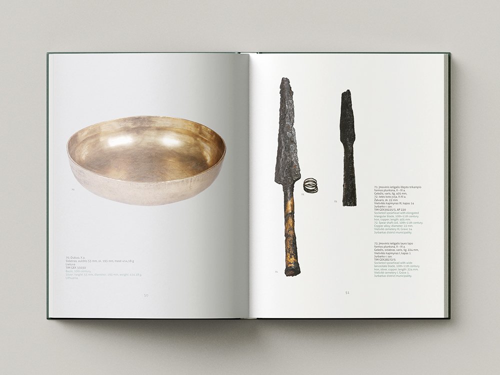 Open catalogue spread with archaeological finds: a shallow silver-coloured bowl on the left page and several dark, corroded iron objects, including spearhead-like pieces and a small spiral, on the right.