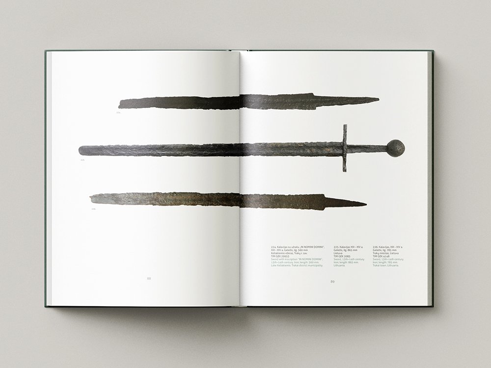 Open archaeology catalogue showing three long archaeological iron weapons laid horizontally across the spread, including a sword with a simple crossguard and round pommel, with catalogue information below.