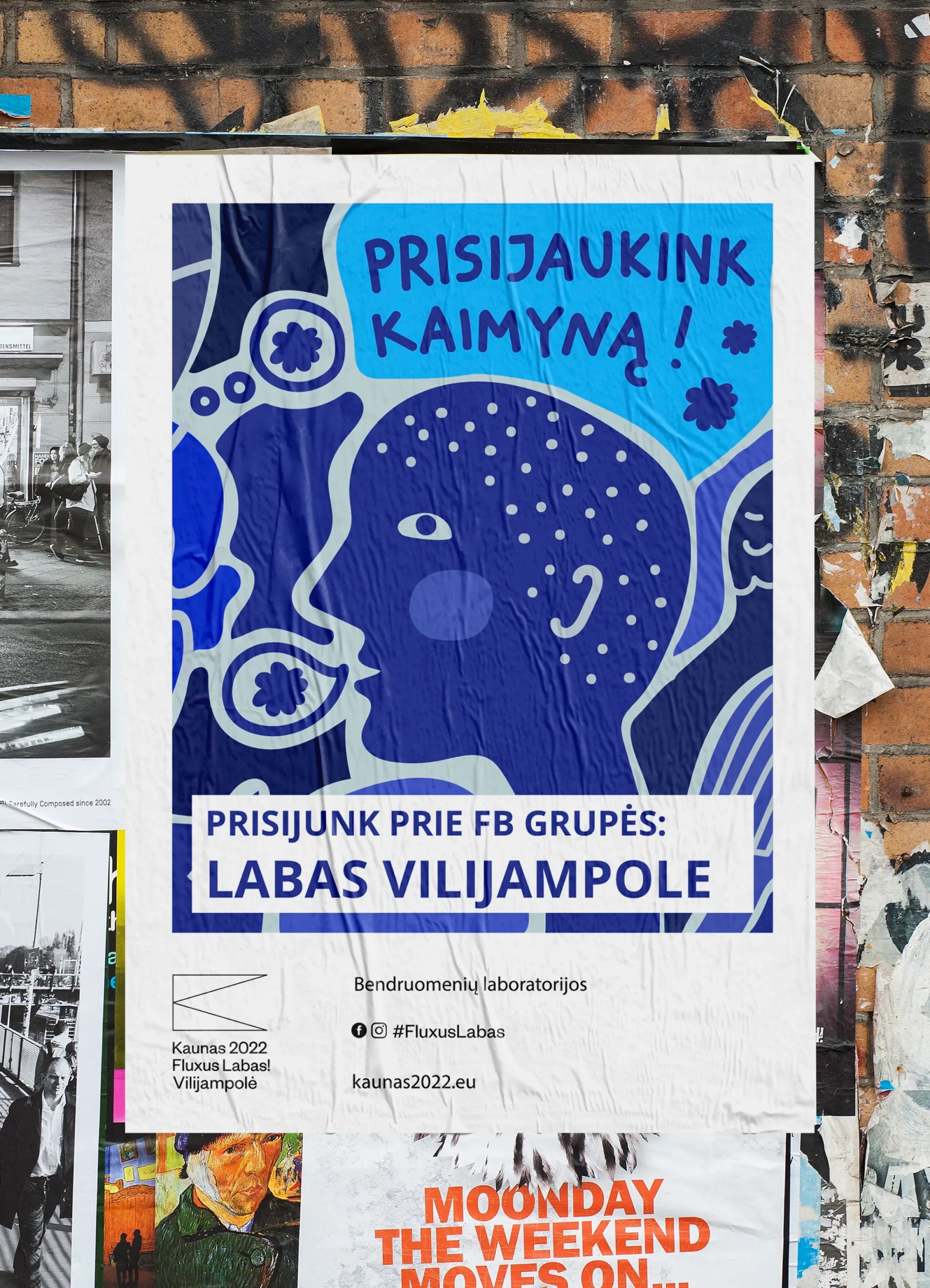 A large blue community poster is pasted onto a weathered brick wall among layers of other posters. Friendly abstract faces, flowers and whimsical creatures crowd together beneath the message “Prisijaukink kaimyną!” (“Get to know your neighbour!”). Below, bold text invites residents to join the Facebook group “Labas Vilijampole.”