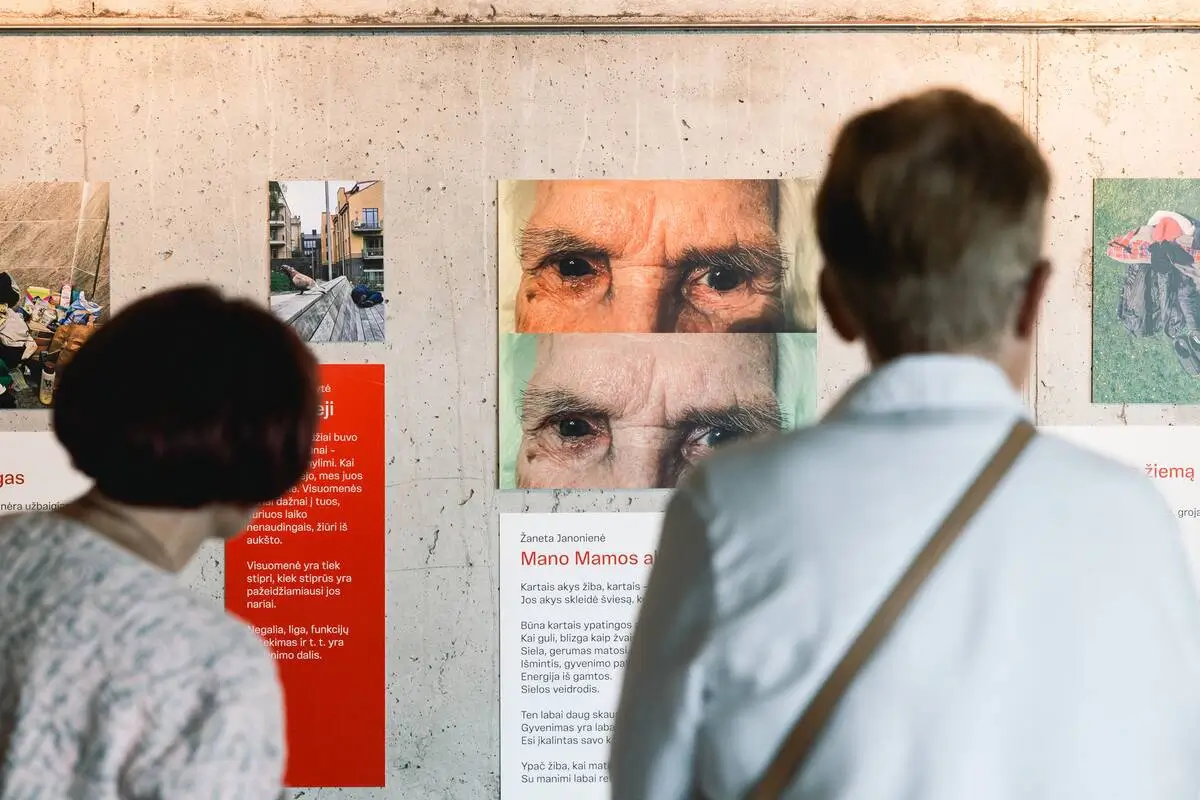Two visitors examining a photographic artwork showing close-ups of an elderly woman's eyes, accompanied by personal reflections.