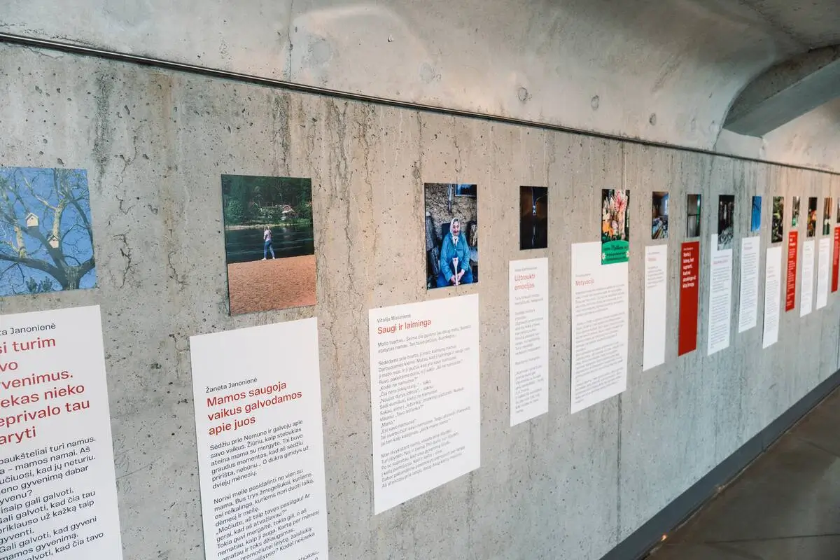 A row of photographs and personal stories about dementia caregiving displayed along a curved concrete exhibition wall.