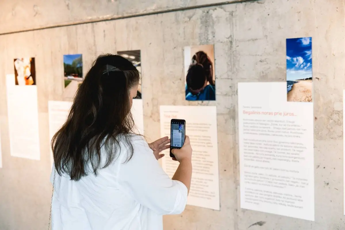 A visitor photographing an exhibition display featuring personal stories and images related to dementia caregiving.