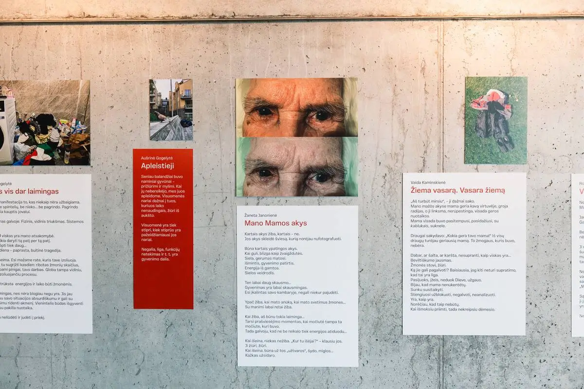 Photographs and personal stories displayed on a concrete wall, including a close-up of an elderly woman's eyes.