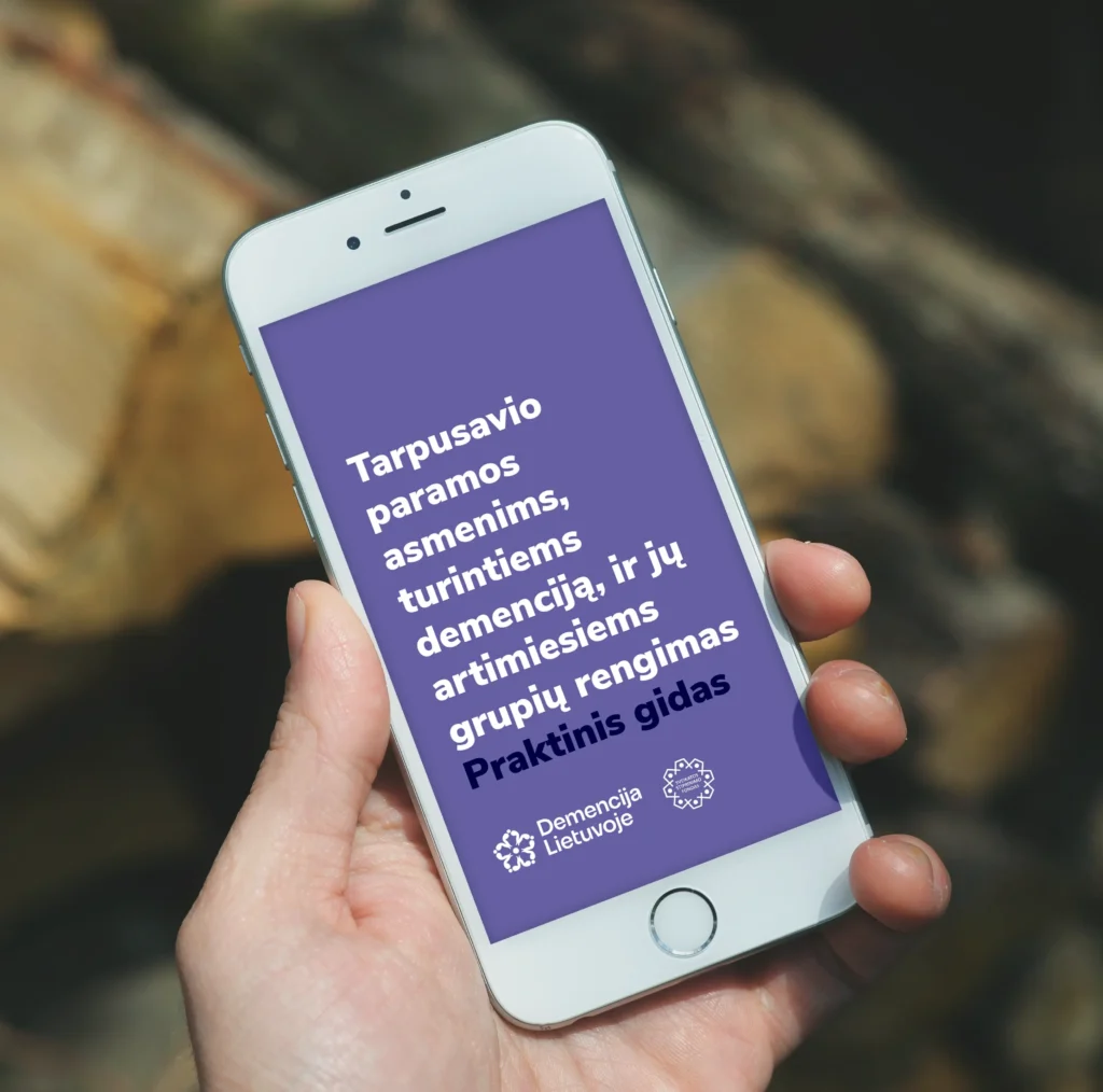 A smartphone displaying the purple cover of an accessible PDF titled “Practical Guide to Organising Peer Support Groups for People Living with Dementia and Their Loved Ones,” featuring the Dementia Lithuania logo.