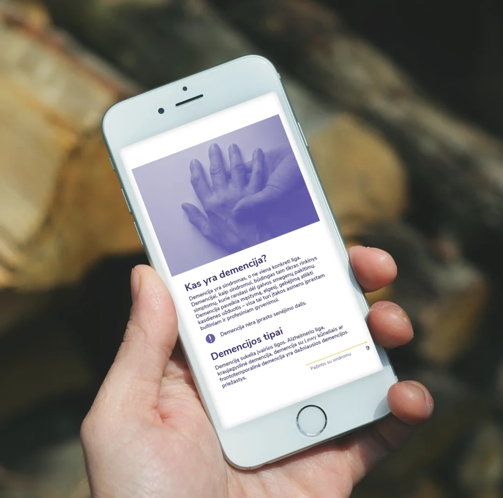 A smartphone displaying a page from an accessible PDF guide, featuring a purple-tinted photograph of hands and information about dementia and its different types.